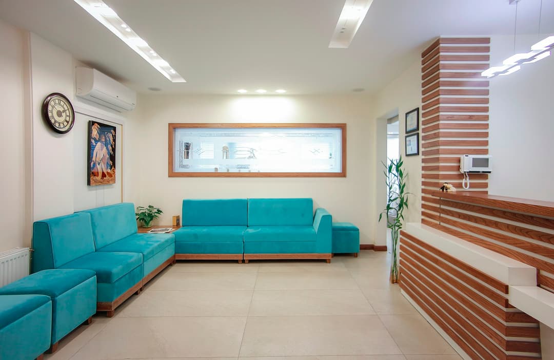 Sala de espera com sofás verde-água, painel de madeira ripada e quadro na parede