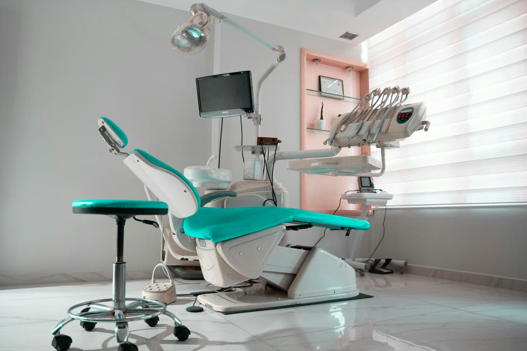 Cadeira odontológica com estofado verde-água e banqueta ao lado, em sala de piso claro