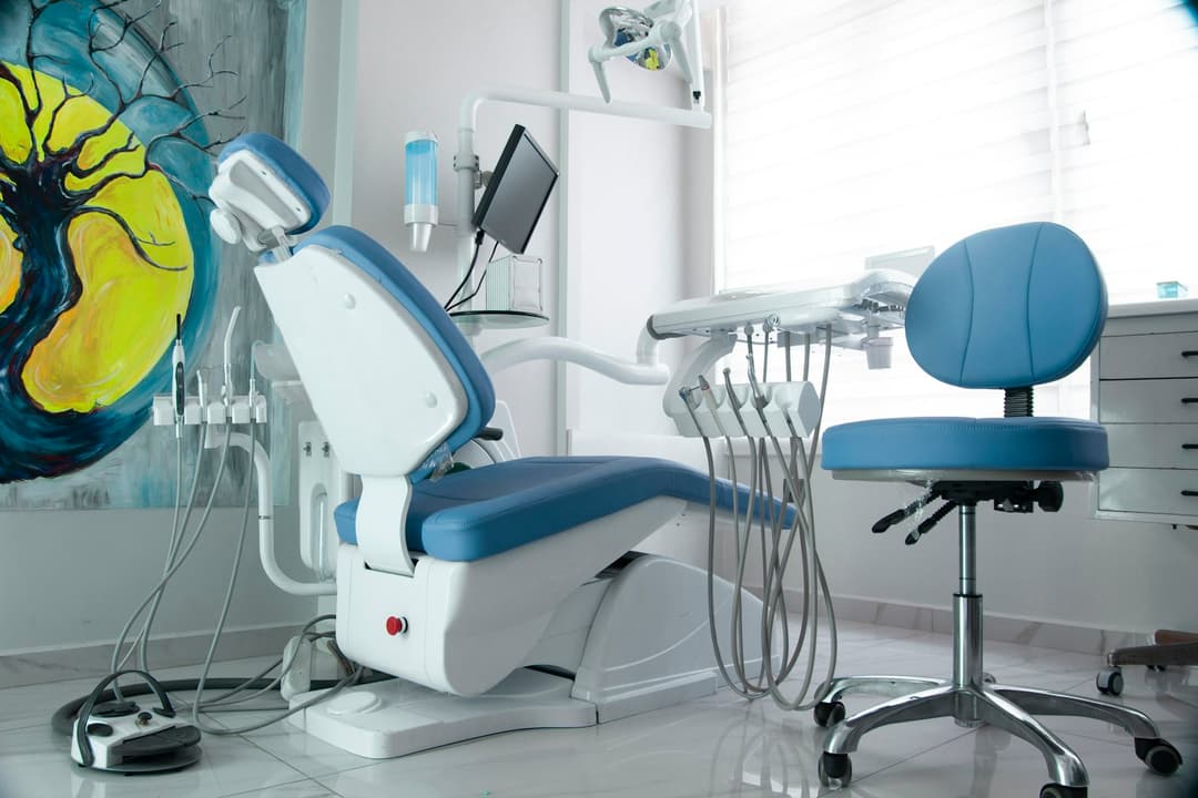 Consultório com cadeira odontológica de estofado azul e um painel colorido de árvore na parede
